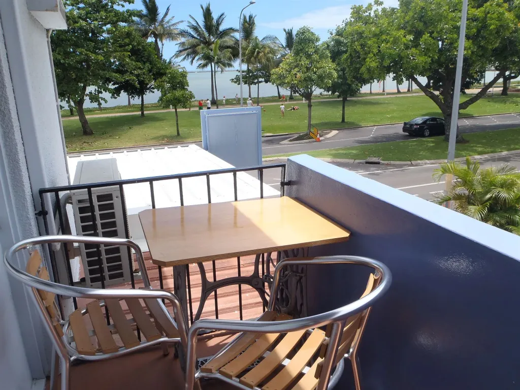 Une table et des chaises en osier sur un balcon avec vue sur un espace vert et la mer.