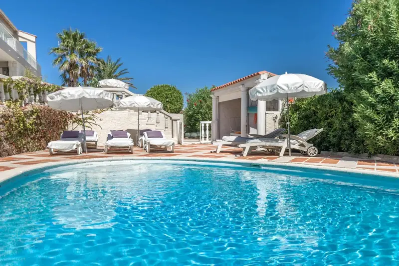 Une piscine bleue bordée de transats blancs sous des parasols.