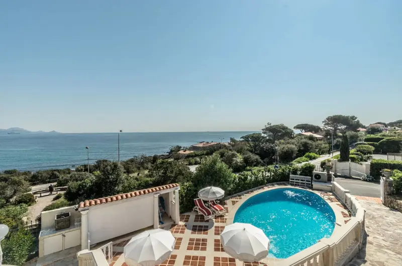 Une piscine avec parasols surplombe la mer et la vegetation.