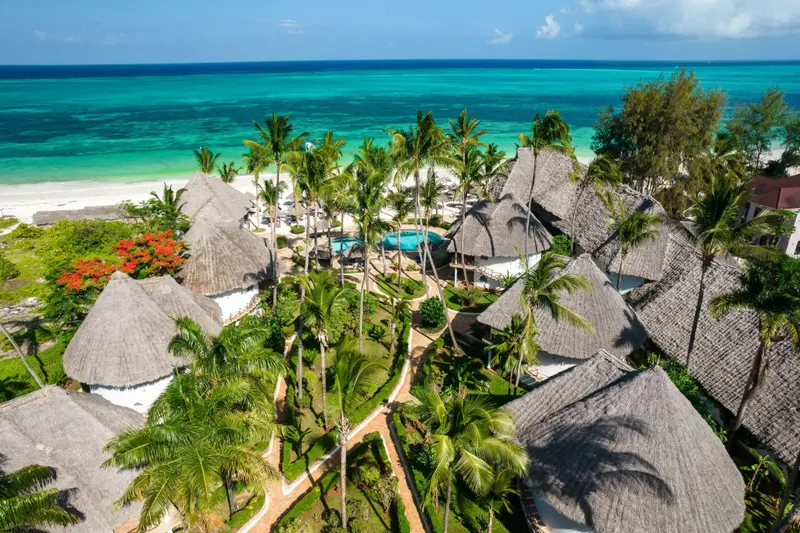 Vue aérienne d'un ensemble de bungalows aux toits de chaume bordant une plage de sable blanc et une mer turquoise.