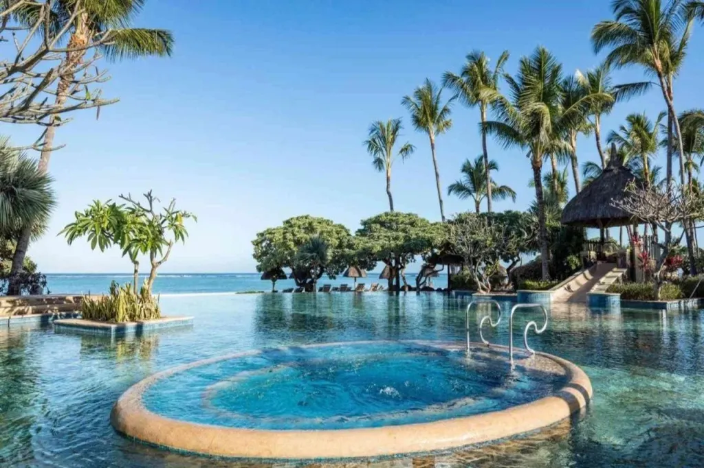 Une piscine à débordement avec un jacuzzi intégré offre une vue sur la mer et la végétation tropicale.