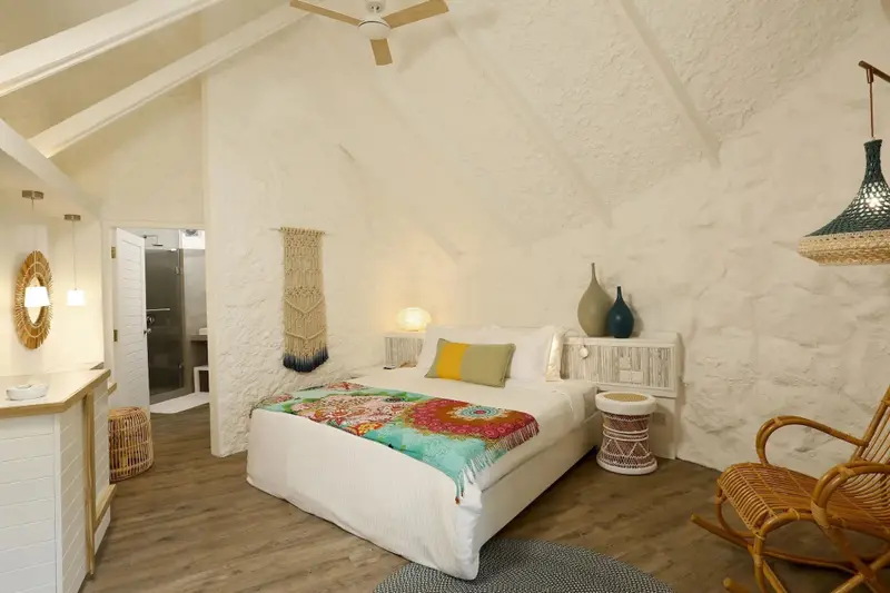 Une chambre lumineuse avec un lit recouvert d'une courtepointe colorée et un fauteuil en osier.