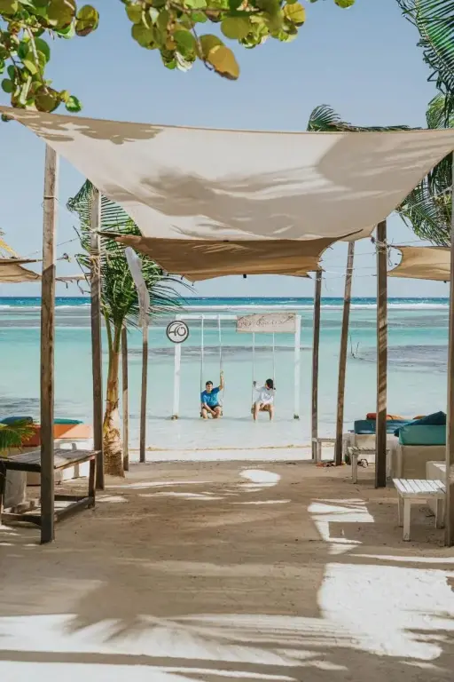 Vue sur une plage de sable blanc avec des transats et des balancelles au bord de l'eau.