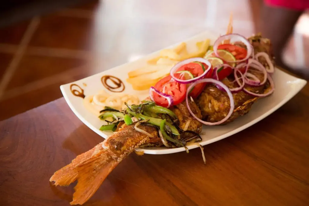 Un poisson frit entier est servi avec des frites et des légumes.