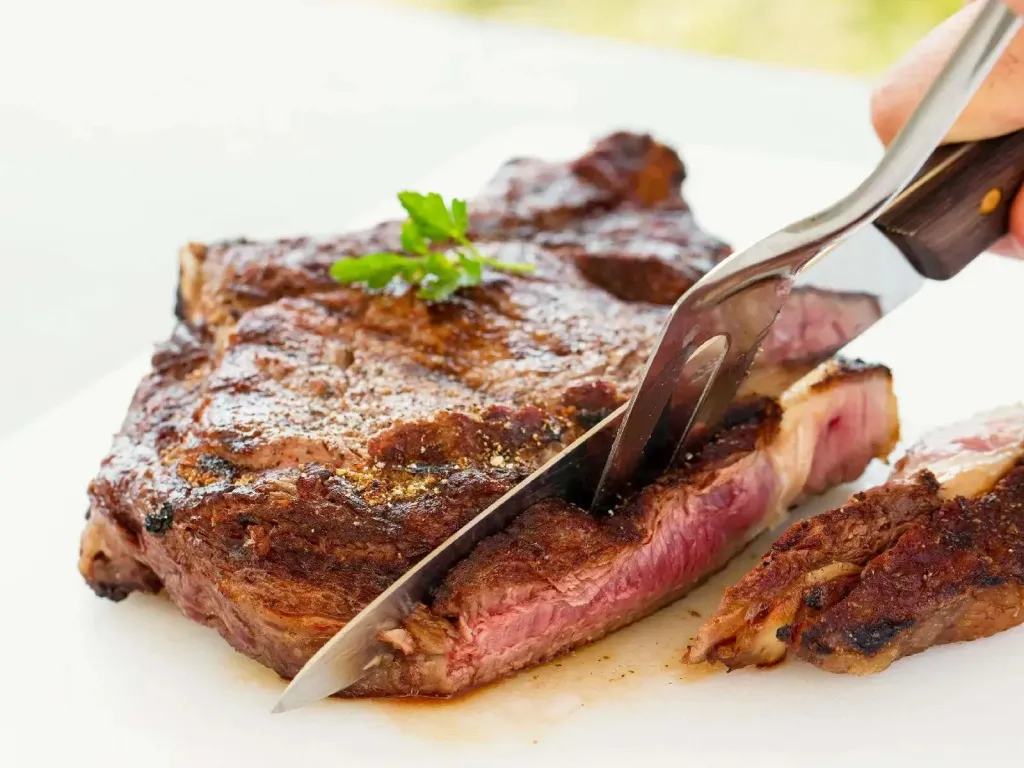 Une viande grillée est coupée avec un couteau sur une assiette blanche.