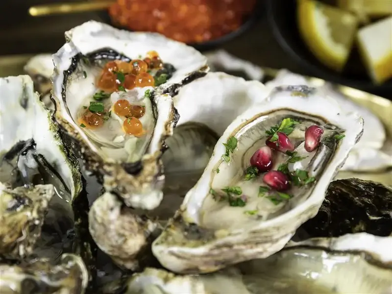 Des huîtres fraîches sont présentées sur un lit de glace pilée, garnies de caviar et d'herbes.
