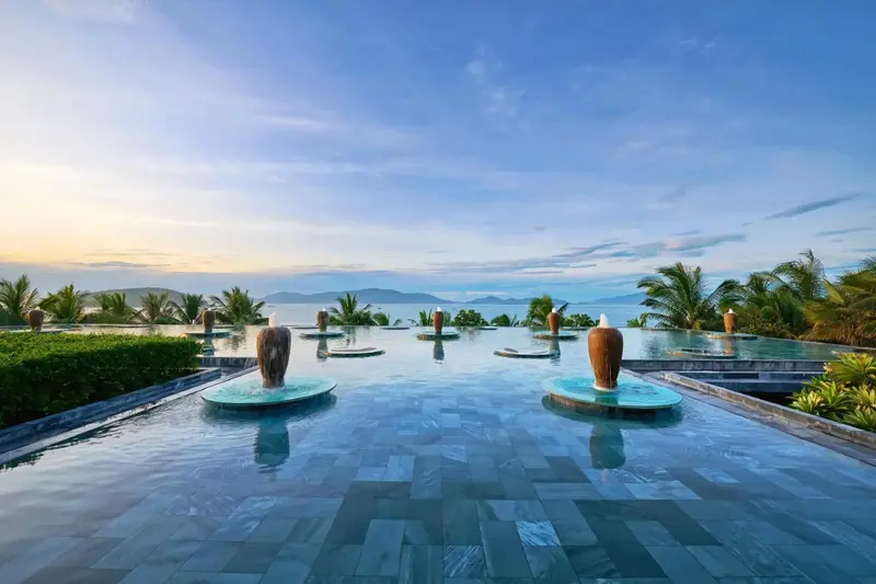 Piscine rectangulaire avec des fontaines et une vue sur la mer au loin.