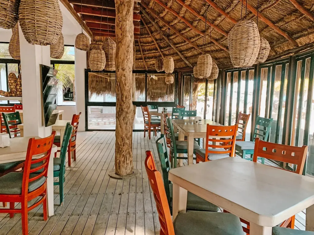 Une salle à manger lumineuse avec des tables et des chaises colorées sous un toit de chaume.