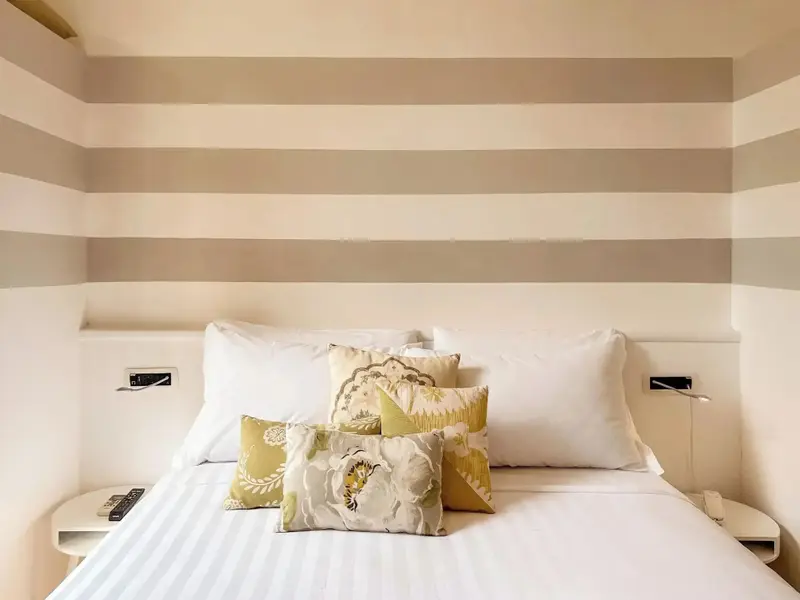 Un lit recouvert de coussins blancs et colorés dans une chambre décorée de rayures horizontales.