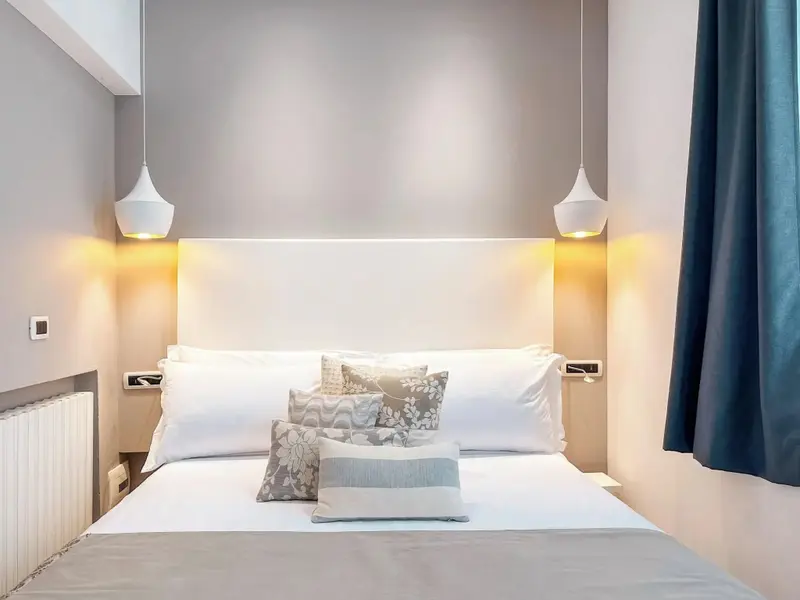 Un lit double est dispose dans une chambre aux murs clairs et aux rideaux bleus.
