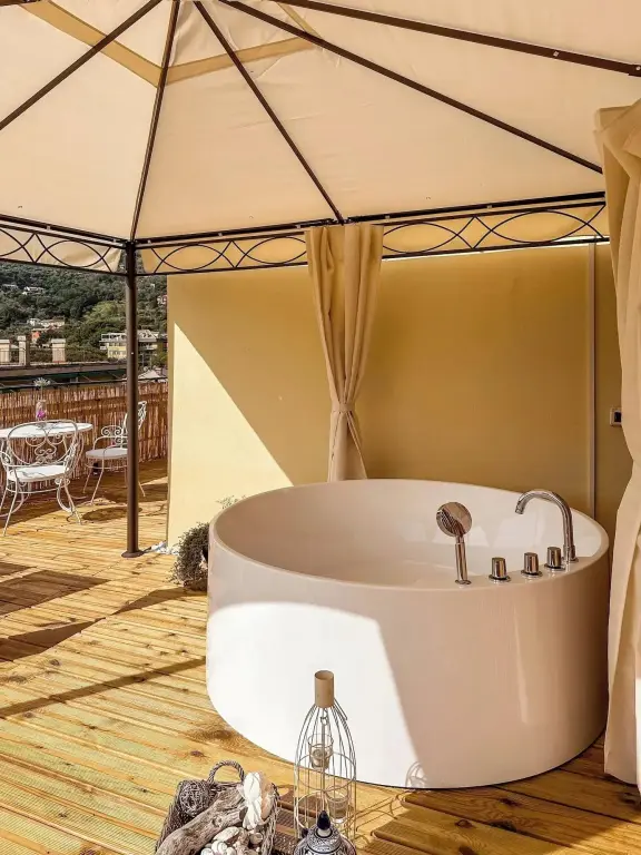 Une baignoire blanche est installée sur une terrasse en bois abritée par un auvent.