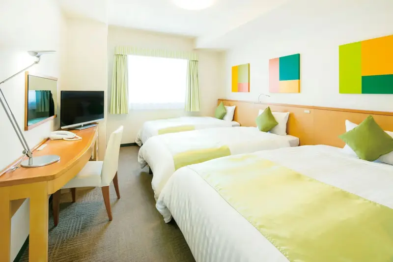 Une chambre lumineuse avec trois lits simples et un bureau près de la fenêtre.