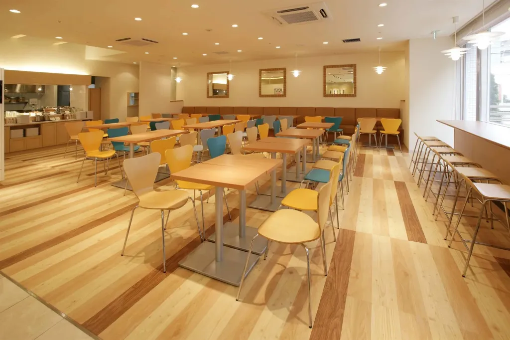Une salle lumineuse avec des tables et des chaises disposées sur un sol en bois clair.