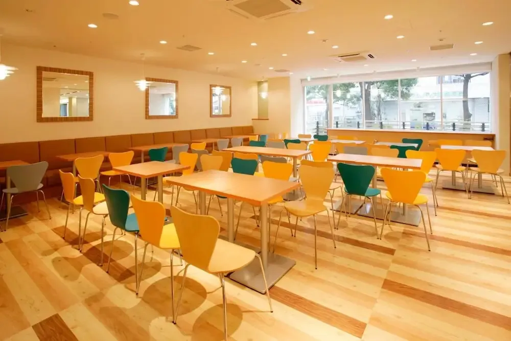 Une salle lumineuse est aménagée avec des tables et des chaises colorées.