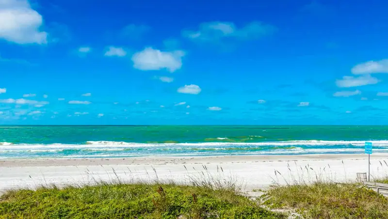 Une plage de sable blanc bordée par une mer turquoise sous un ciel bleu nuageux.