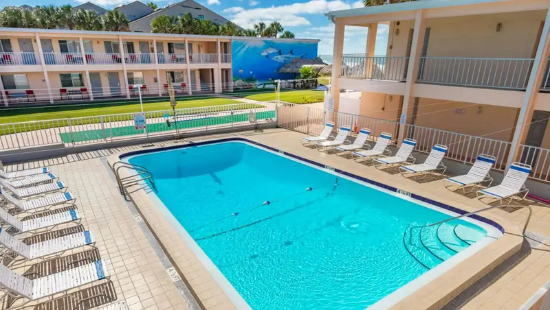 Une piscine rectangulaire turquoise est entourée de chaises longues bleues et blanches.