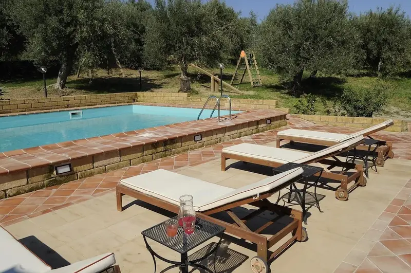 Transats alignés au bord d'une piscine rectangulaire ensoleillée.