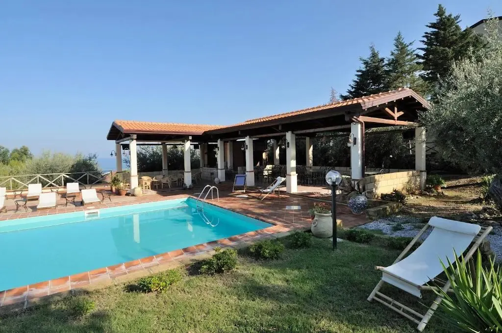 Une piscine turquoise bordée d'une terrasse ombragée et d'un jardin verdoyant.