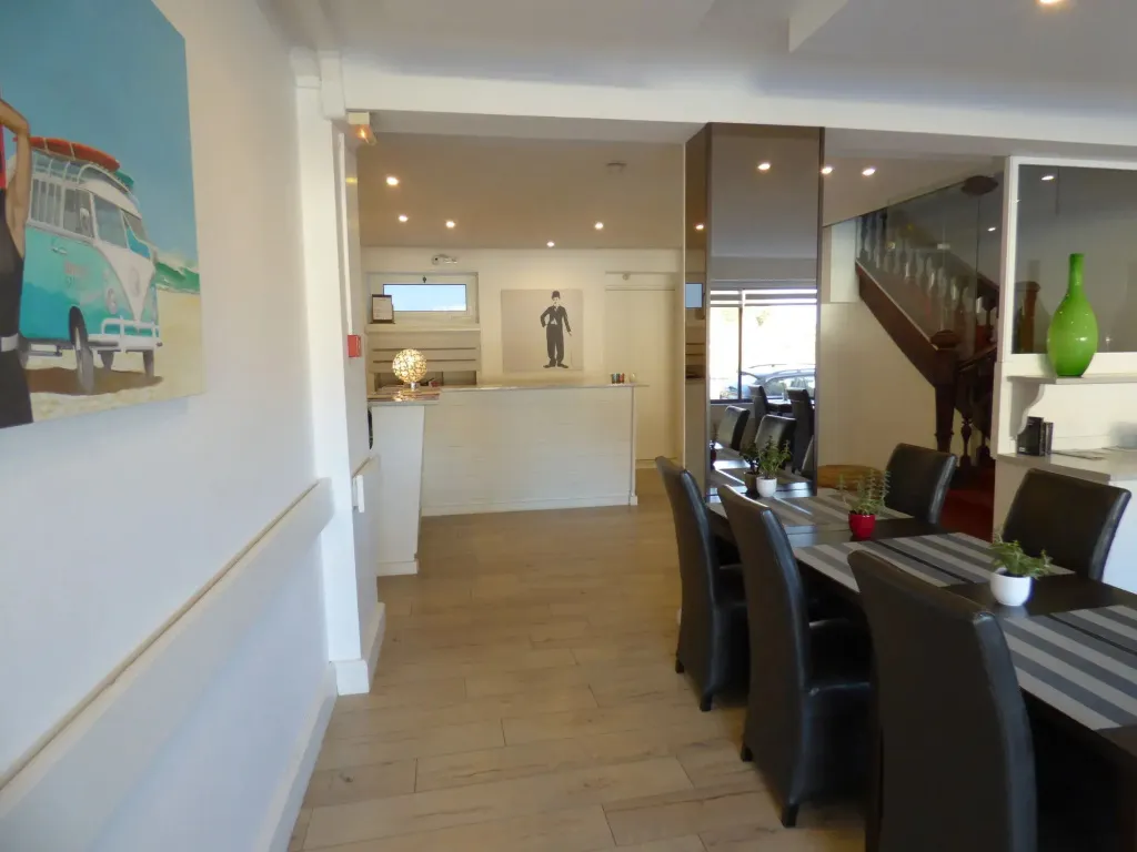 Une salle à manger lumineuse avec des tables dressées et un escalier en fond.