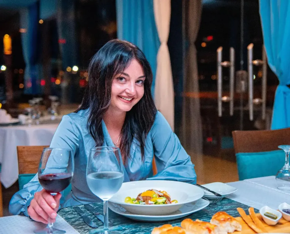 Une femme souriante est assise à une table dressée avec des plats et des verres.