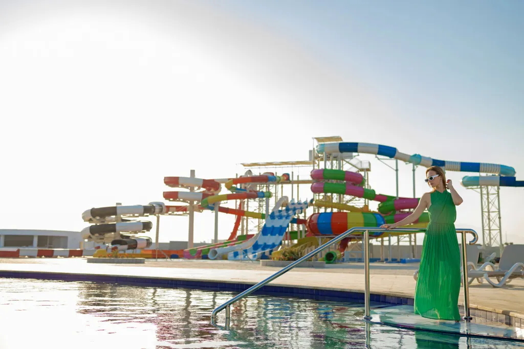 Une femme se tient près d'une piscine avec des toboggans colorés en arrière-plan.