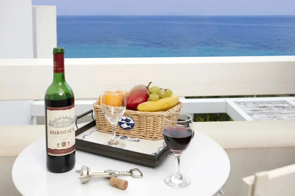 Une table blanche avec une bouteille de vin, des fruits et des verres, devant une vue sur la mer.