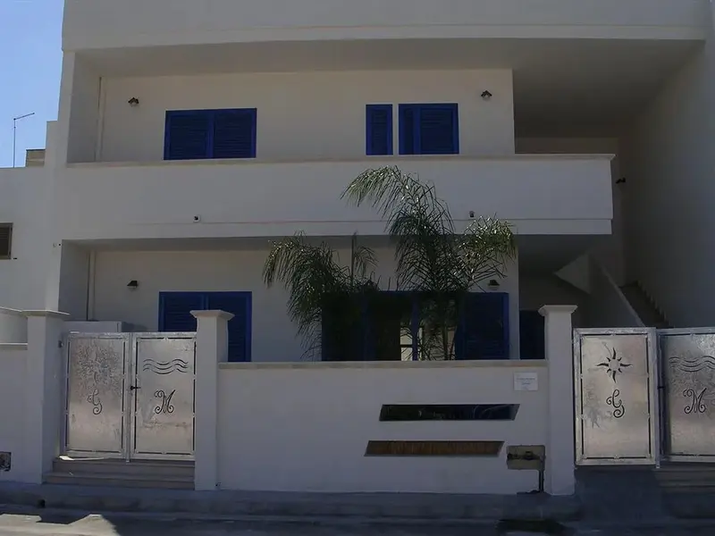Facade blanche d'un bâtiment avec des ouvertures bleues et une palmeraie.