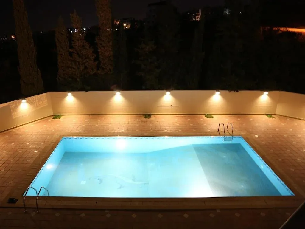 Piscine rectangulaire éclairée la nuit, entourée d'une terrasse carrelée.