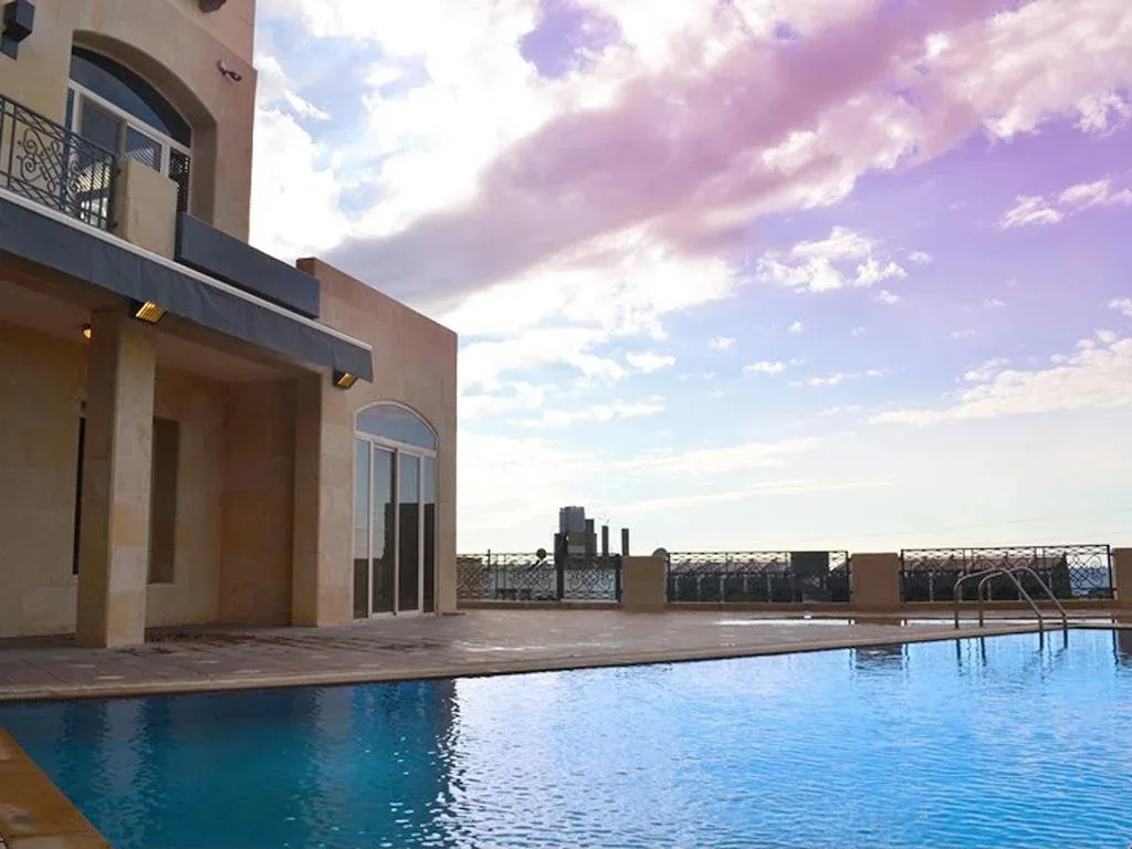 Une piscine bleue reflète un ciel nuageux et un bâtiment beige.