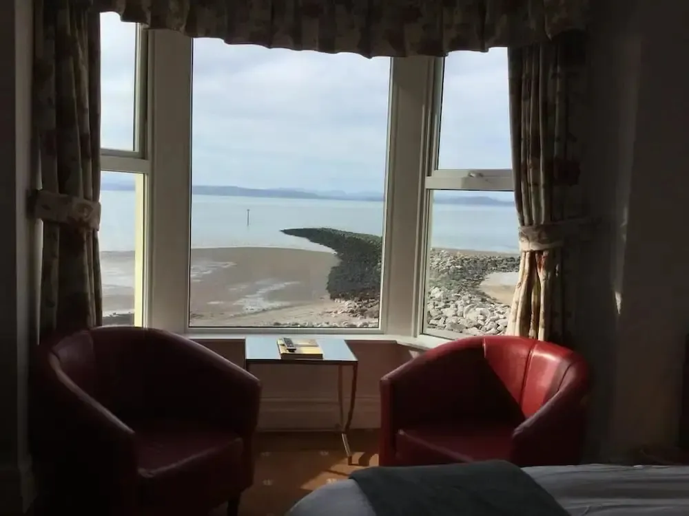 Deux fauteuils rouges sont placés devant une grande fenêtre donnant sur la mer et la plage.