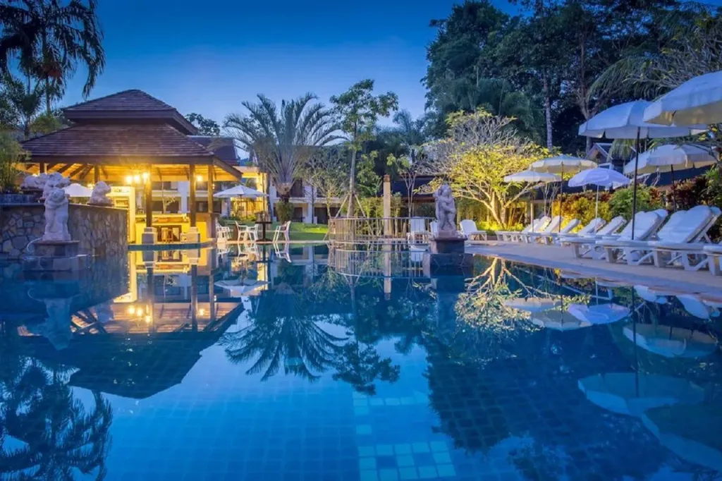 Une piscine illuminée reflète un bâtiment et des palmiers au crépuscule.