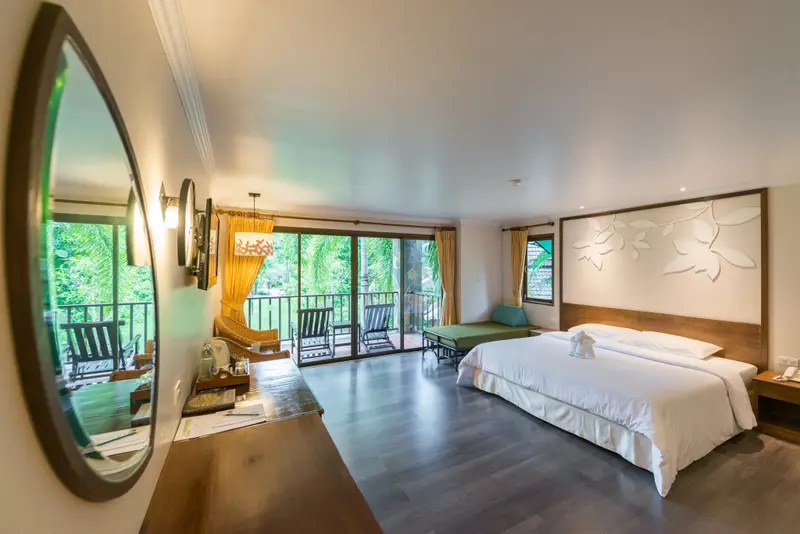 Une chambre lumineuse avec un grand lit et un balcon donnant sur la végétation.