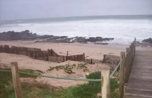 Une plage de sable s'étend vers une mer agitée sous un ciel gris.