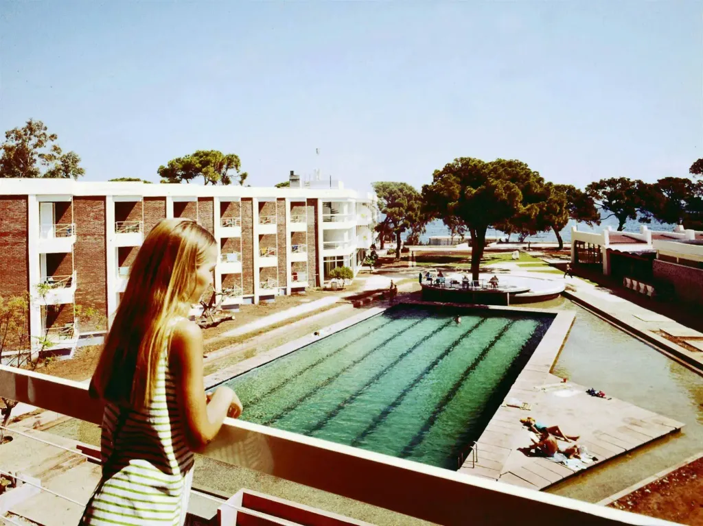 Une femme regarde une piscine et un bâtiment en arrière-plan.