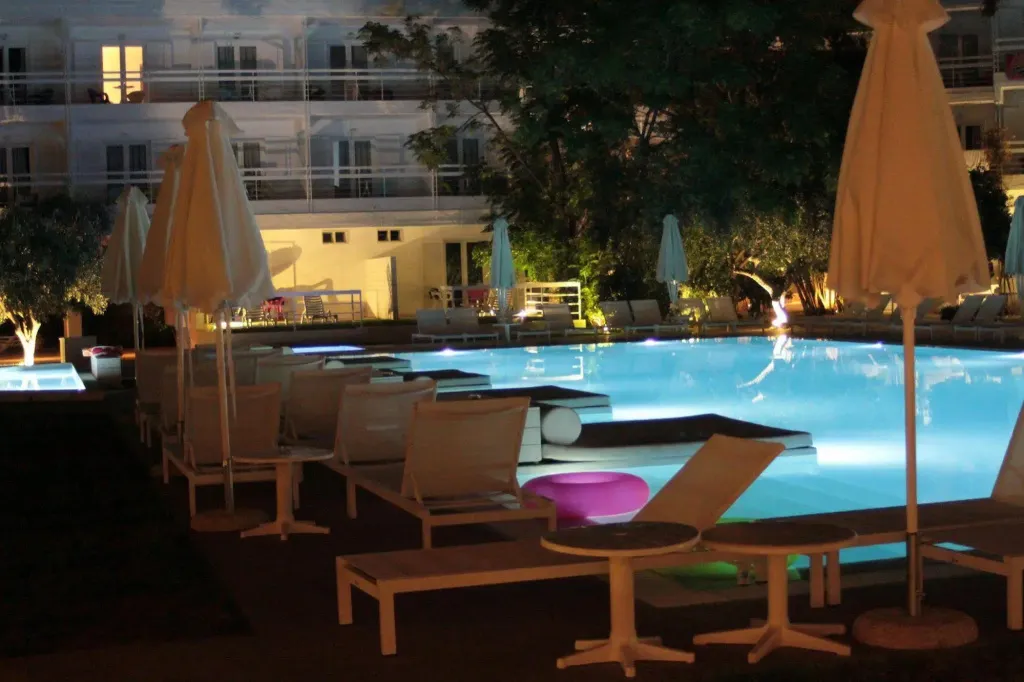 Transats blancs disposés autour d'une piscine illuminée la nuit.