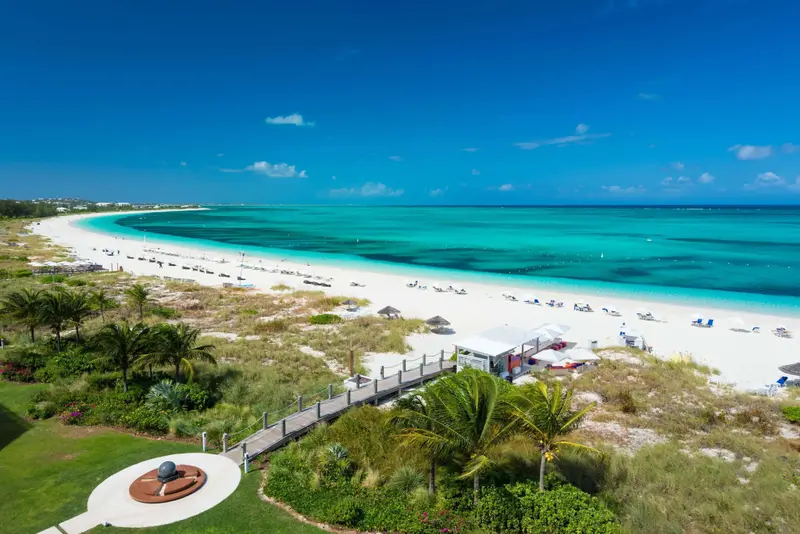 Vue aérienne d'une plage de sable blanc bordée d'une mer turquoise et de végétation luxuriante.