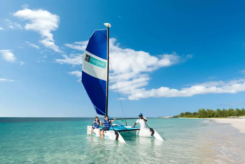Un catamaran bleu navigue sur une eau turquoise sous un ciel clair.