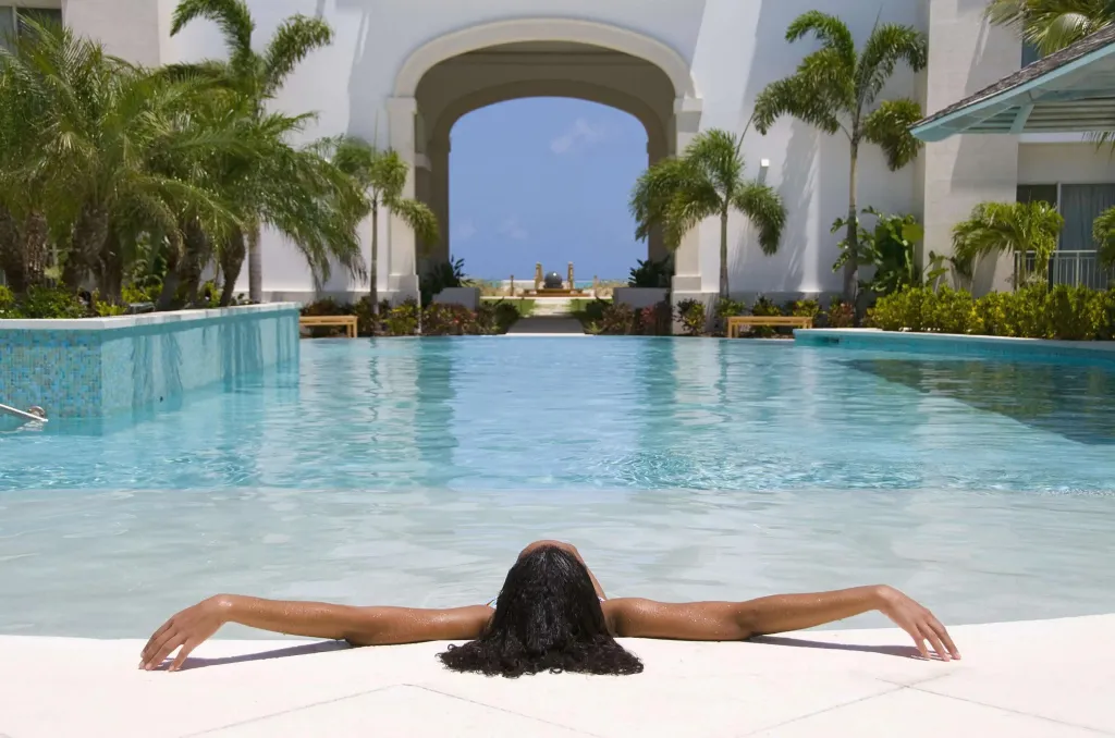 Une personne se détend à la surface d'une piscine rectangulaire bordée d'une terrasse.