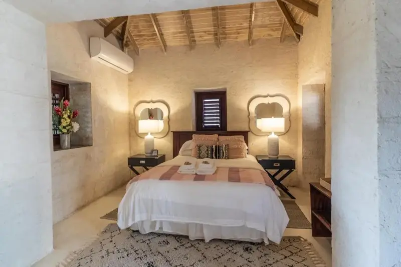Une chambre lumineuse avec un lit recouvert d'une courtepointe et de coussins.