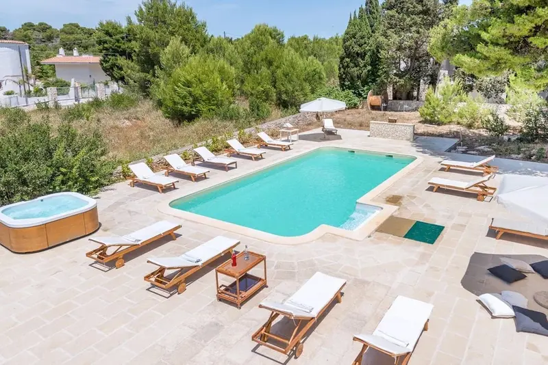 Une piscine rectangulaire bordée de transats et d'un jacuzzi, entourée de végétation.