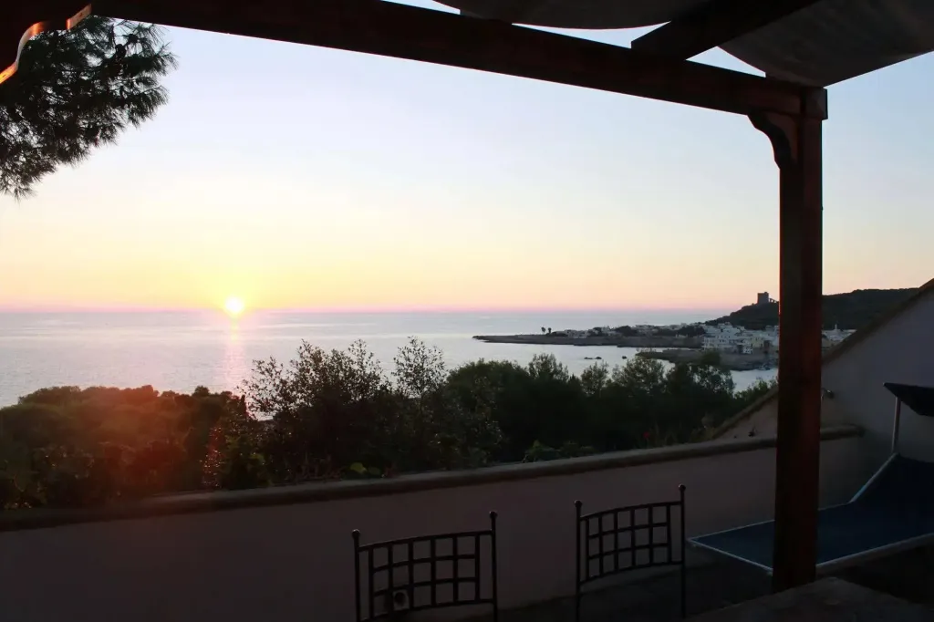 Vue sur la mer au coucher du soleil depuis une terrasse ombragée.