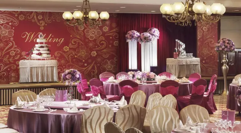 Une salle de réception décorée pour un mariage avec des tables rondes dressées et des arrangements floraux.