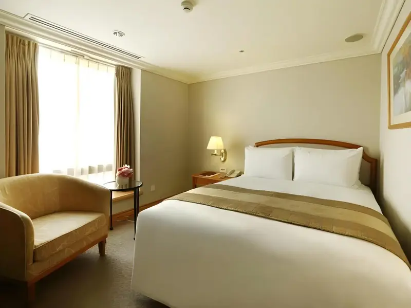 Une chambre lumineuse avec un lit double et un fauteuil.