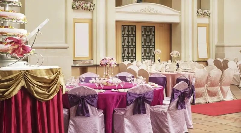 Une salle de réception élégante est mise en scène avec des tables dressées et des décorations florales.