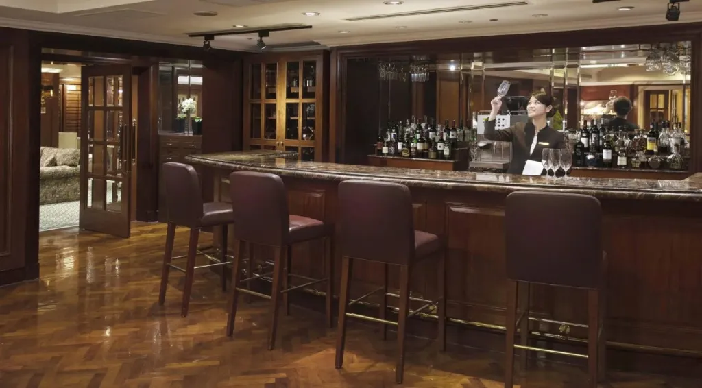 Un barman prépare un cocktail derrière un comptoir en bois sombre.