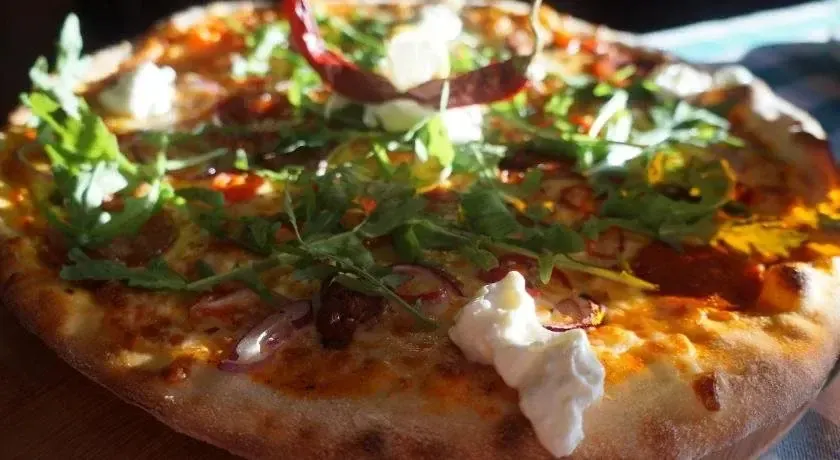 Une pizza généreusement garnie de légumes et de fromage est présentée sur une planche à découper en bois.