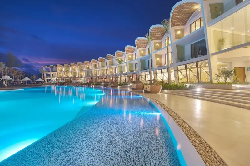 Piscine illuminée devant un bâtiment aux lignes courbes et modernes.