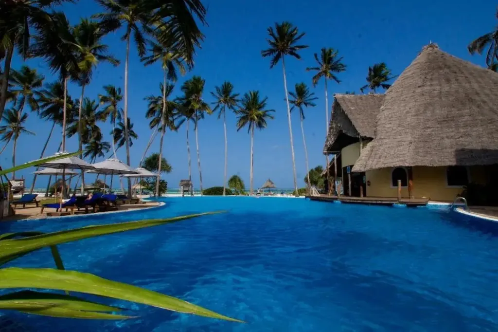 Une piscine bleue bordée de transats sous des palmiers.