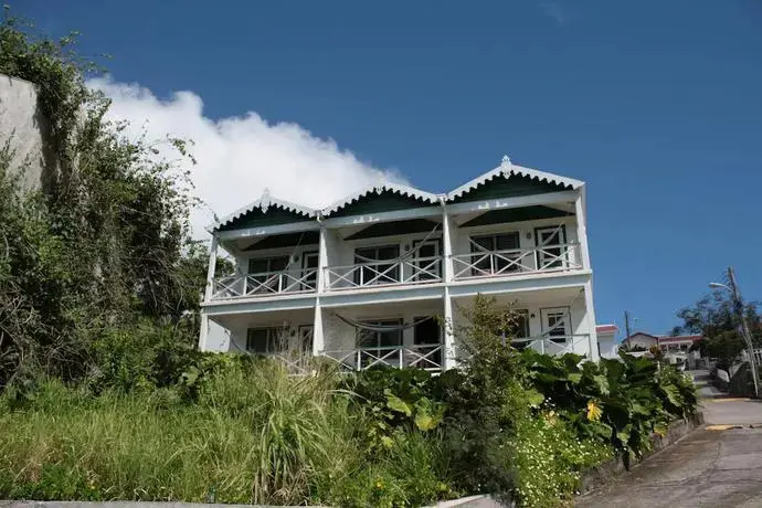 Bâtiment blanc à deux étages avec des balcons et une végétation luxuriante.