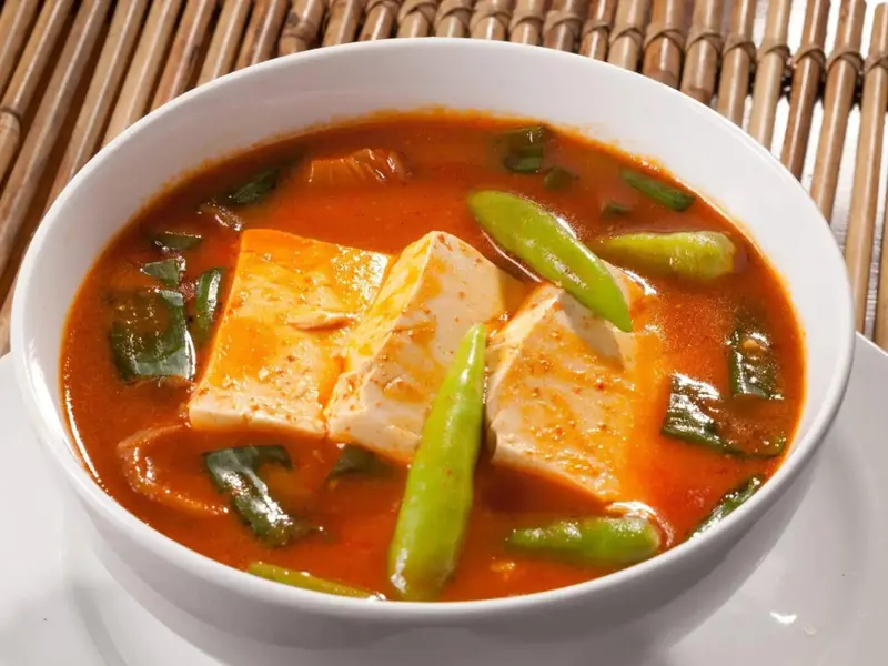 Un bol de soupe épicée avec du tofu et des légumes verts.